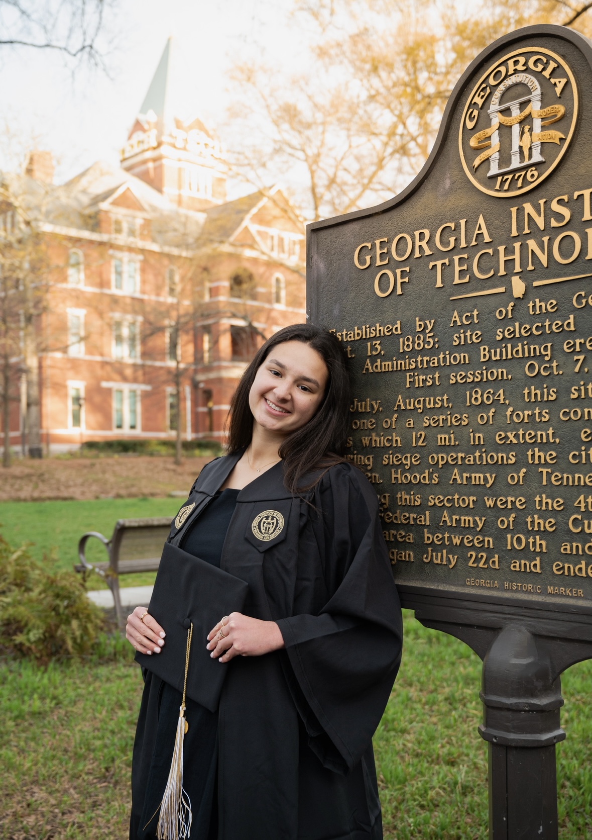 Elianna, wearing a graduation gown, leans against the Georgia Tech sign.